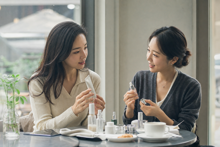 Two Korean women comparing skincare notes over coffee in Seoul