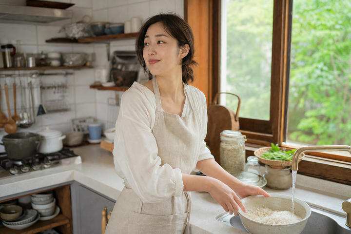 A candid Korean woman rinsing rice in a sunlit Korean kitchen